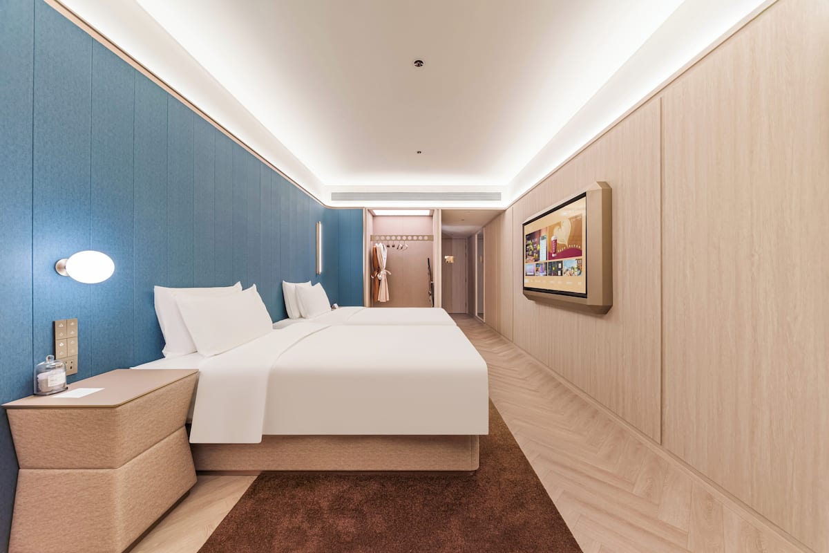 Een moderne hotelkamer met een groot bed, nachtkastjes, een tv aan de muur en een gang naar een badkamer.