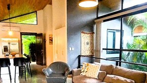 Un soggiorno moderno con divano, poltrona e tavolino. Sullo sfondo, una zona pranzo con sedie e tavolo.