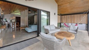 Un'ampia zona giorno con mobili in vimini, un tavolino in legno e un'ampia porta vetrata scorrevole che dà su un balcone con un'amaca.