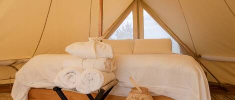 A tent with a bed, rolled towels, and a woven lantern.
