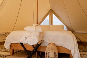Ein Zelt mit einem Bett, zusammengerollten Handtüchern und einer gewebten Laterne.