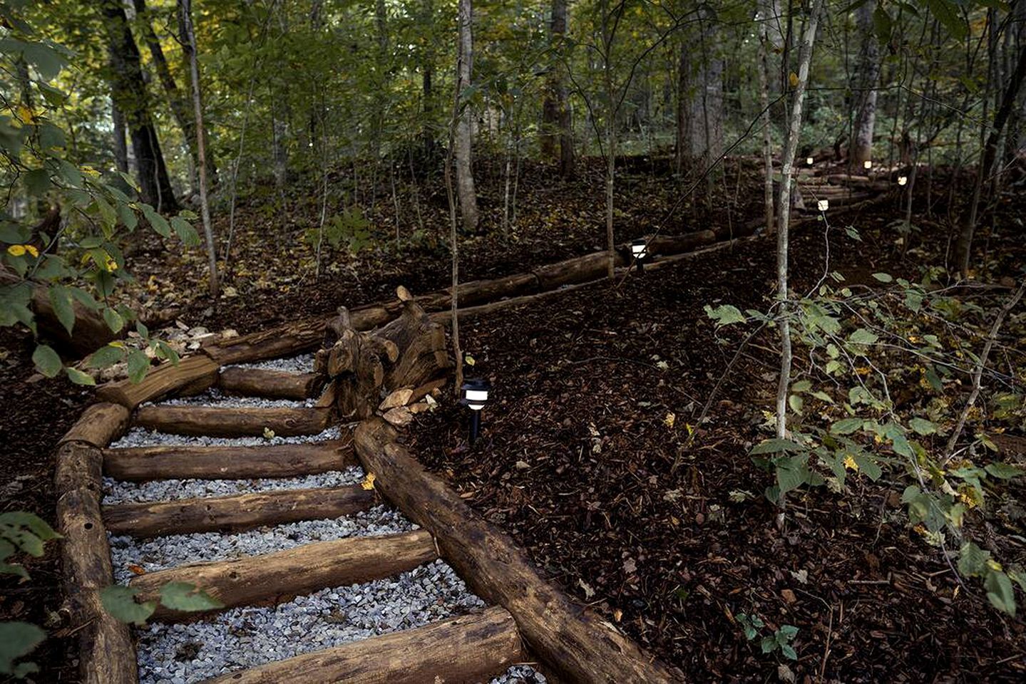 A wooden spiral staircase in a forested area with gravel steps.