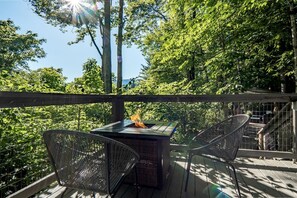 Una terraza exterior con un hogar, sillas de mimbre y vistas a árboles.