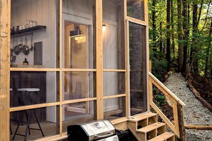 Une cabane en bois avec un coin cuisine, un tabouret de bar et un barbecue à l’extérieur.
