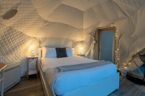 A bedroom with a quilted dome ceiling, a bed with a blue blanket, bedside lamps, and a heater.