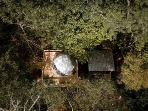 An aerial view of a cabin surrounded by dense foliage, with a circular structure and a rectangular building.
