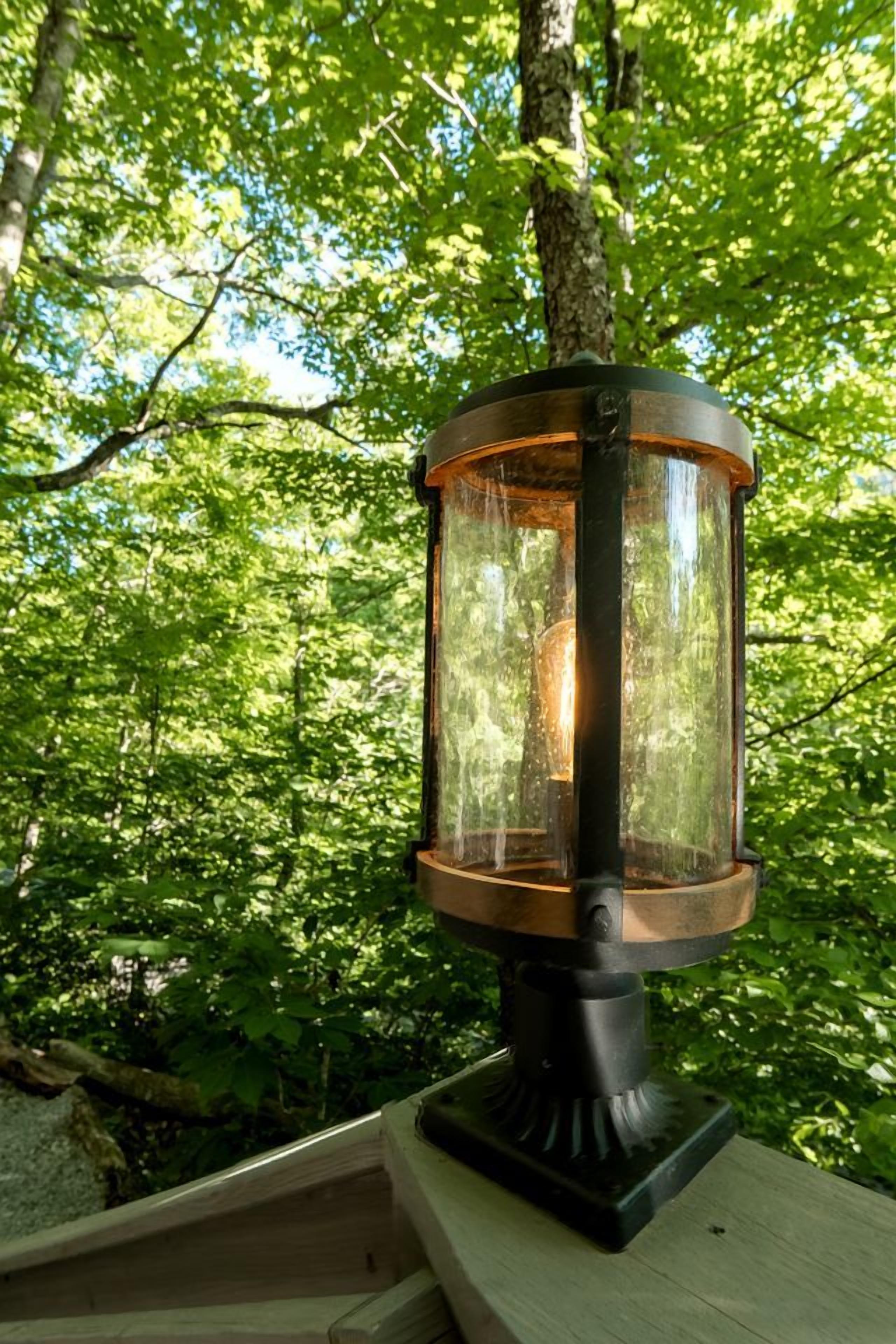En lyktliknande lampa som är monterad på en trästolpe i ett skogsområde.