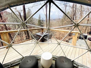 Una estructura de domo geodésico con cubierta de madera, asientos al aire libre y vista del bosque circundante.