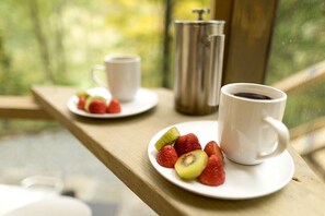 A breakfast setup with a cup of coffee, a plate of strawberries and kiwi, and a thermos on a wooden table by a window. - Experience Unrivaled Luxury: Exclusive Dome with Hot Tub and Unique Views in North Carolina (Todd)