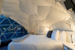 A cozy, tent-like bedroom with a large bed, a bedside table, and a view through a geometric window.