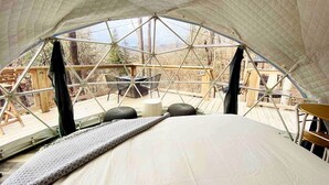 A tented accommodation with a bed, a table, and chairs outside.