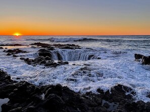 A coastal scene with waves crashing against rocks and a sunset in the background.