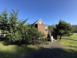 Un chalet rustique en bois, doté d’un toit en pente, entouré d’une végétation luxuriante et accessible par un chemin de gravier.