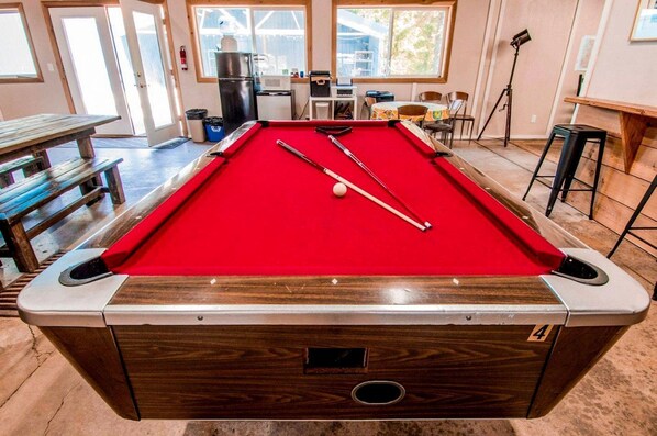 Une table de billard recouverte d’un drap de feutre rouge, un queue et une bille de billard.