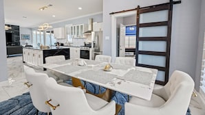 Una cocina moderna con armarios blancos, encimera de mármol y comedor con mesa y sillas blancas.