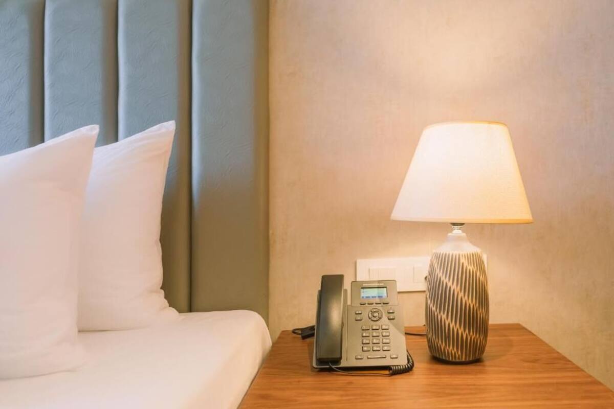 A hotel room with a bed, a bedside telephone, and a lamp on a wooden nightstand.