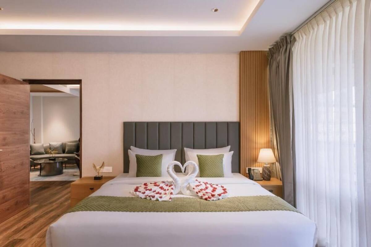 A hotel room with a bed, a nightstand, a lamp, and a view of a dining area.