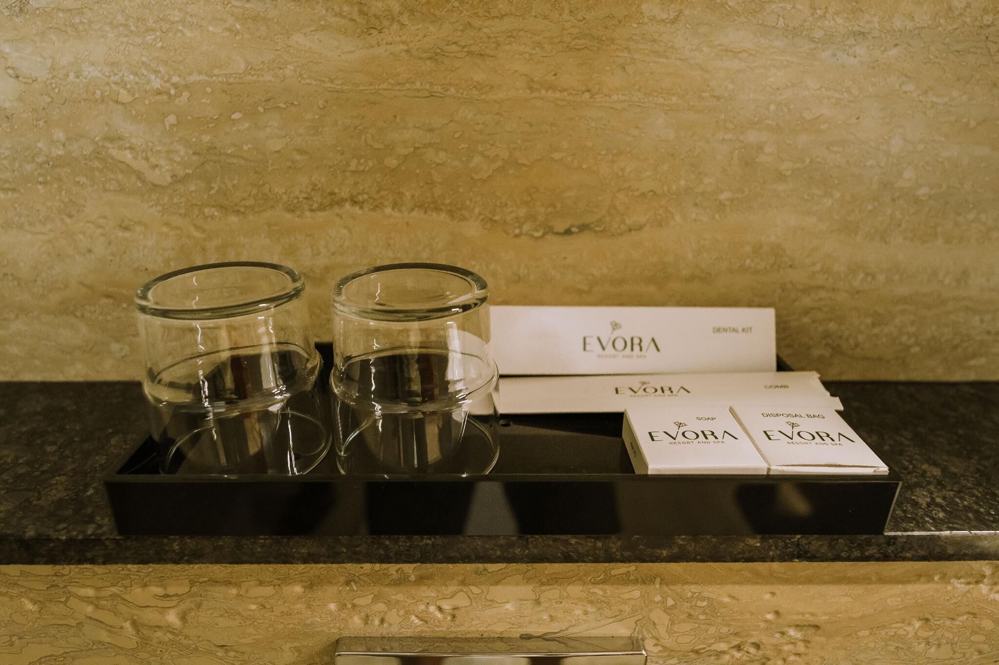 A hotel minibar with Evora branded items including two glasses, a box, and a pack of soap.