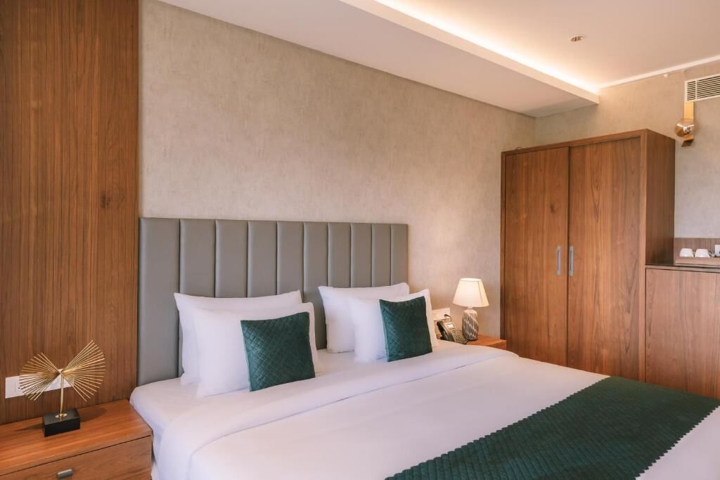 A hotel room with a bed, nightstand, lamp, and wooden wardrobe.