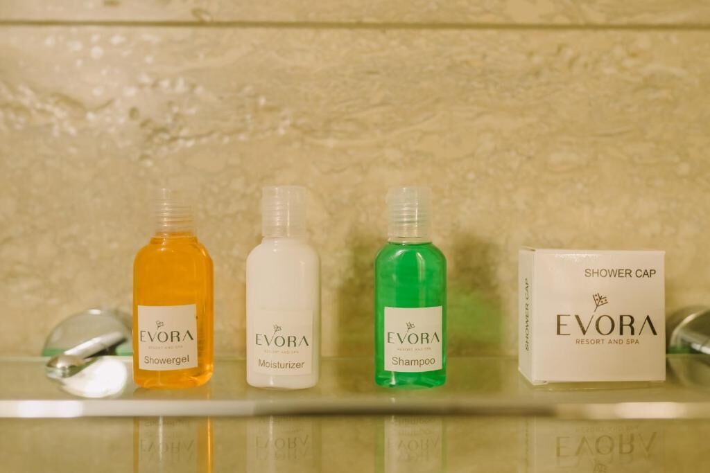 Tres botellas de gel de ducha, crema hidratante y champú Evora, junto con un gorro de ducha sobre una encimera de baño.