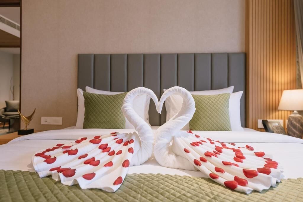 A hotel room with a bed, pillows, a headboard, a bedside table, and a lamp.