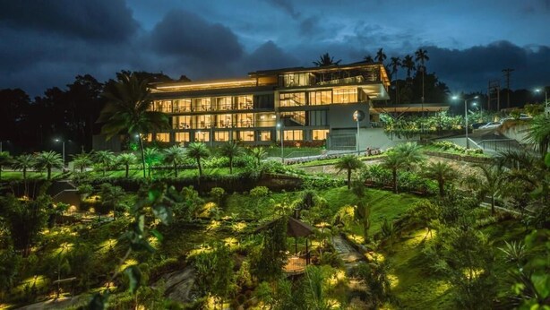 A modern hotel with a large glass facade, a well-maintained garden, and a pool area.