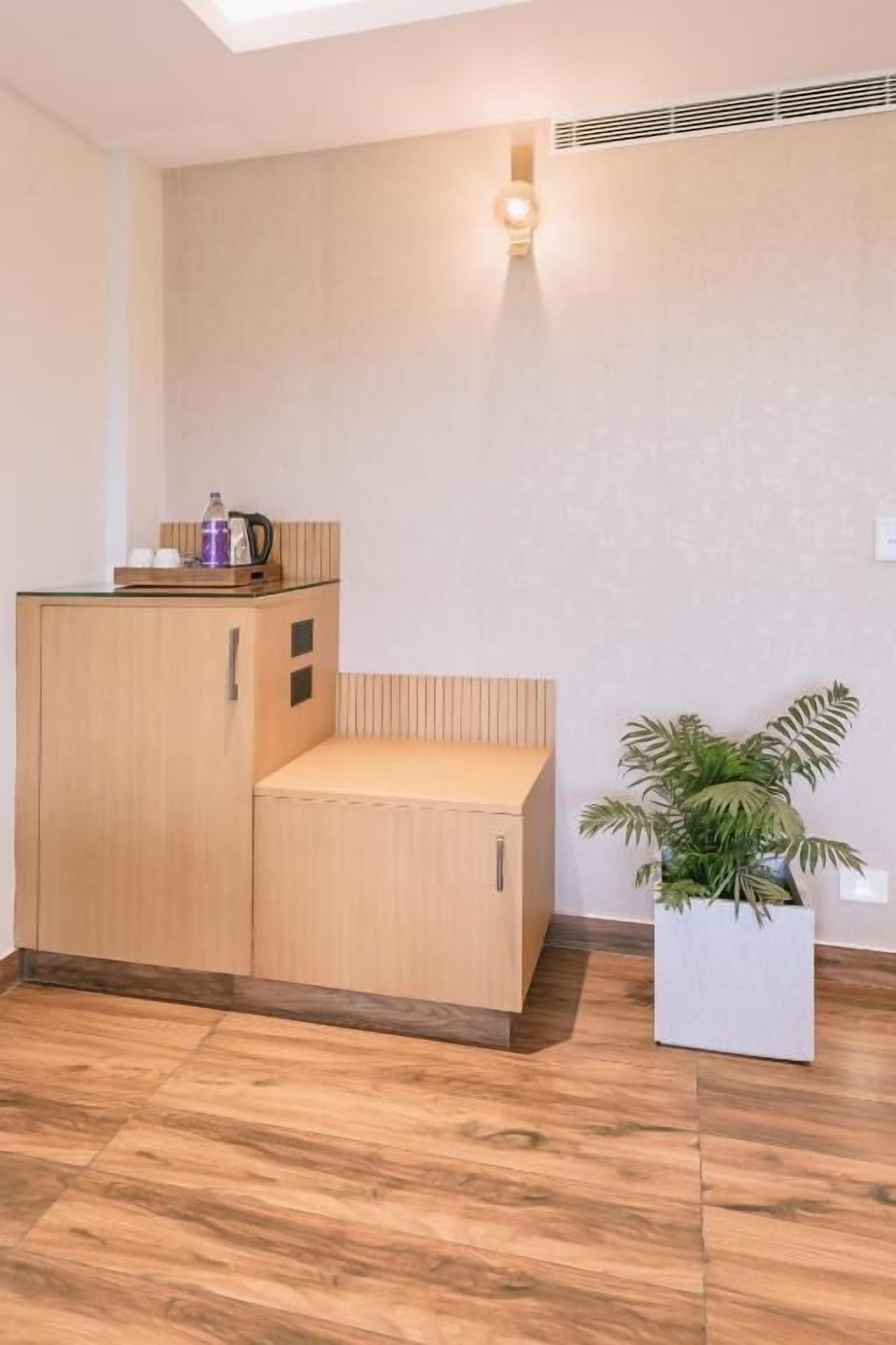 A compact room with a kitchenette, a potted plant, and a ceiling vent.