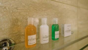 Et badeværelse med en glashylde, der indeholder fire flasker Evora produkter: shower gel, moisturizer og shampoo.