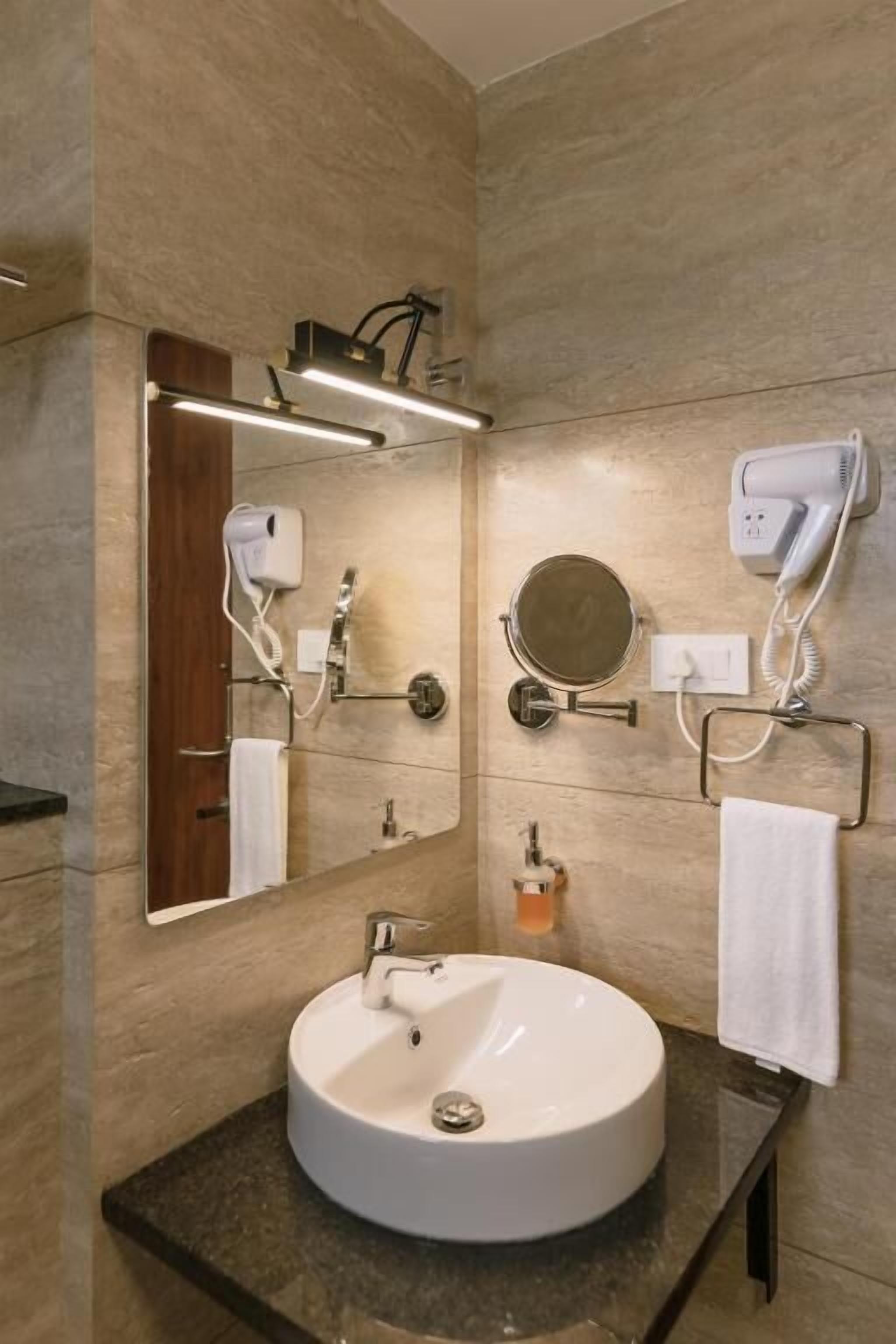 Een moderne badkamer met een rond wastafel, een spiegel, een haardroger en een handdoekhouder.