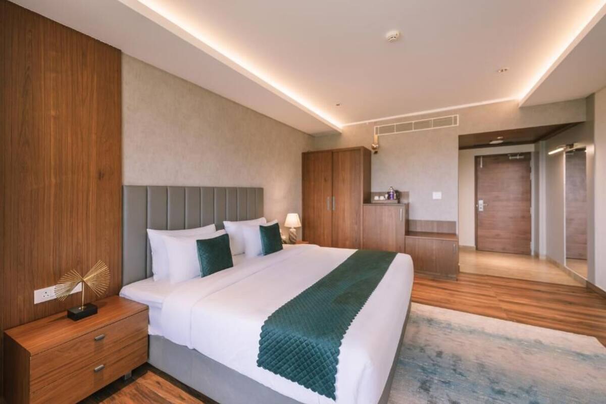 A modern hotel room with a large bed, wooden wardrobe, and a small kitchenette.