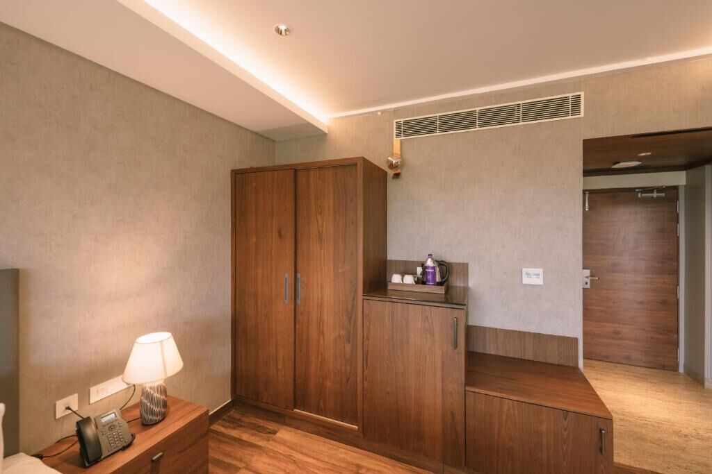 A hotel room with a wooden wardrobe, a bedside table with a lamp, and a small cabinet.