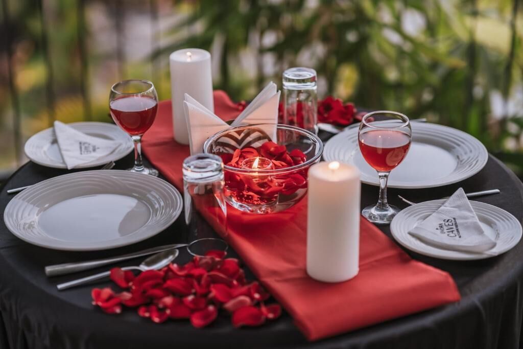Une table dressée pour deux personnes, avec des assiettes, des verres, une bougie et des pétales de rose.