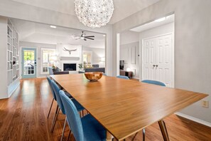 A spacious dining area with a long wooden table, blue chairs, a chandelier, and a fireplace. - Nordic-Inspired Getaway | Hot Tub + Fire Pit (North Richland Hills)