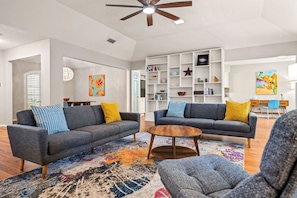 A spacious living room with two grey sofas, a coffee table, and a bookshelf filled with books and decorative items. - Nordic-Inspired Getaway | Hot Tub + Fire Pit (North Richland Hills)