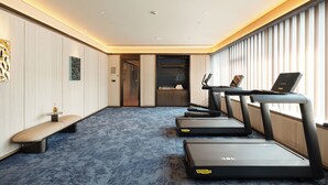 Habitación de hotel con una cinta de correr, un banco y vistas a la ciudad.