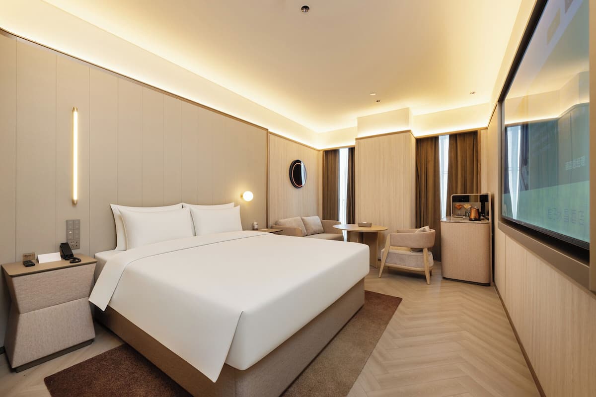 Una habitación de hotel moderna con una cama grande, una mesita de noche, un escritorio pequeño, una silla y una pantalla de televisión.