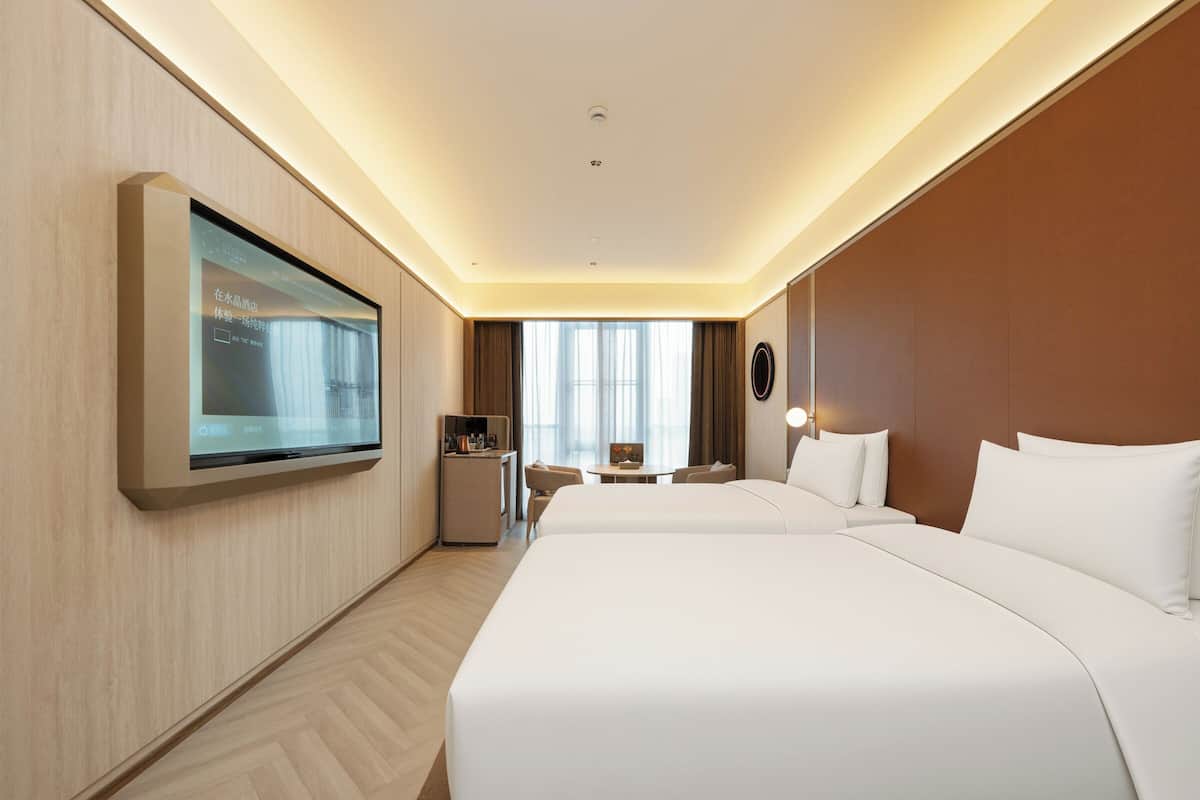 Una habitación de hotel con una cama grande, un escritorio, una silla, un televisor montado en la pared y una ventana con cortinas.