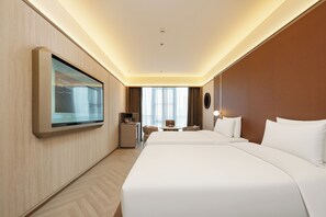 Quarto de hotel com cama grande, escrivaninha, cadeira, televisão na parede e janela com cortinas.