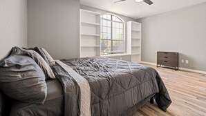 Un dormitorio con cama, ventilador de techo, ventana con persianas y cómoda.