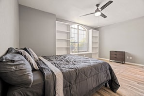 A bedroom with a bed, a ceiling fan, a window with blinds, and a dresser. - Extended Stay Comfort | Prime Location + Garage (Carrollton)