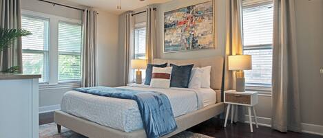 A bedroom with a bed, bedside tables, a ceiling fan, a painting, and a window with curtains.