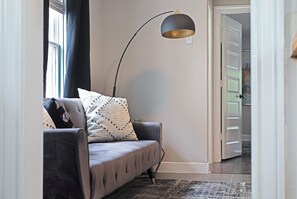 Ein modernes Wohnzimmer mit einem grauen Sofa, einer schwarzen Stehlampe und einem Kissen mit Muster.