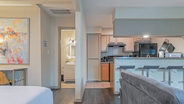 Een moderne hotelkamer met een bed, een groot abstract schilderij, een kitchenette en een barhoek.