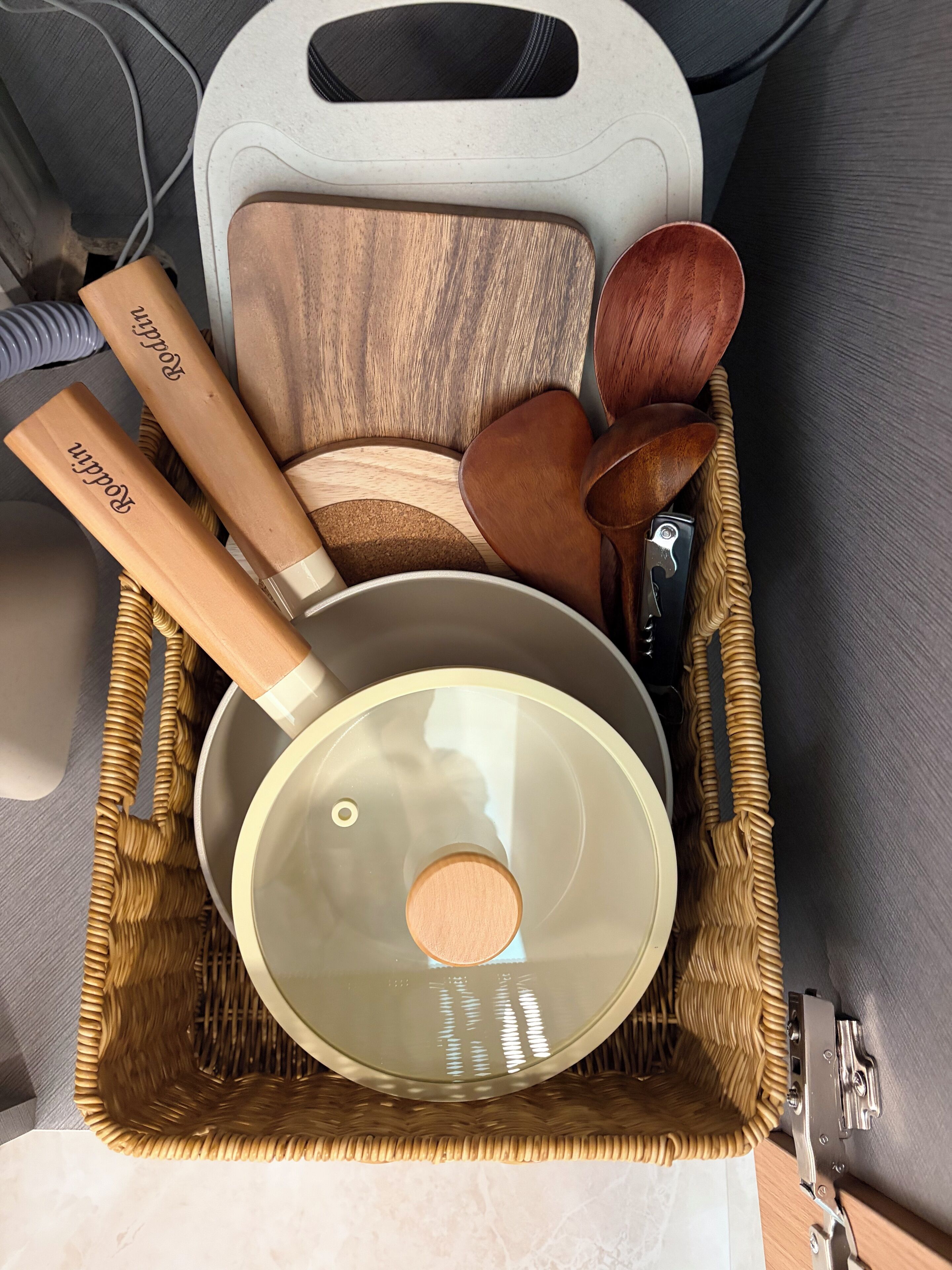 A kitchen storage basket with wooden utensils, a pot, and a cutting board.