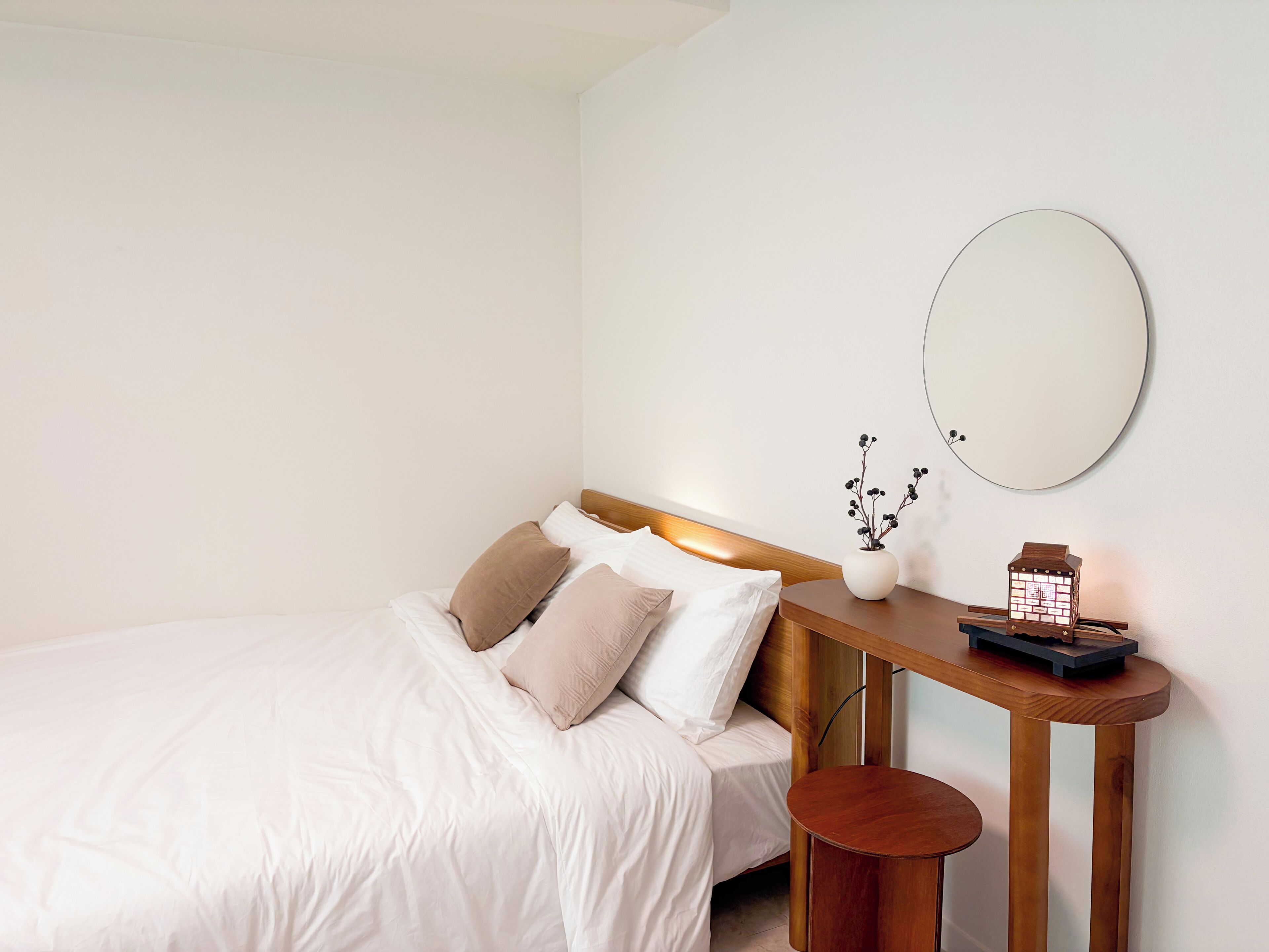 A neatly made bed with pillows, a bedside table with a lamp, and a wall-mounted mirror.