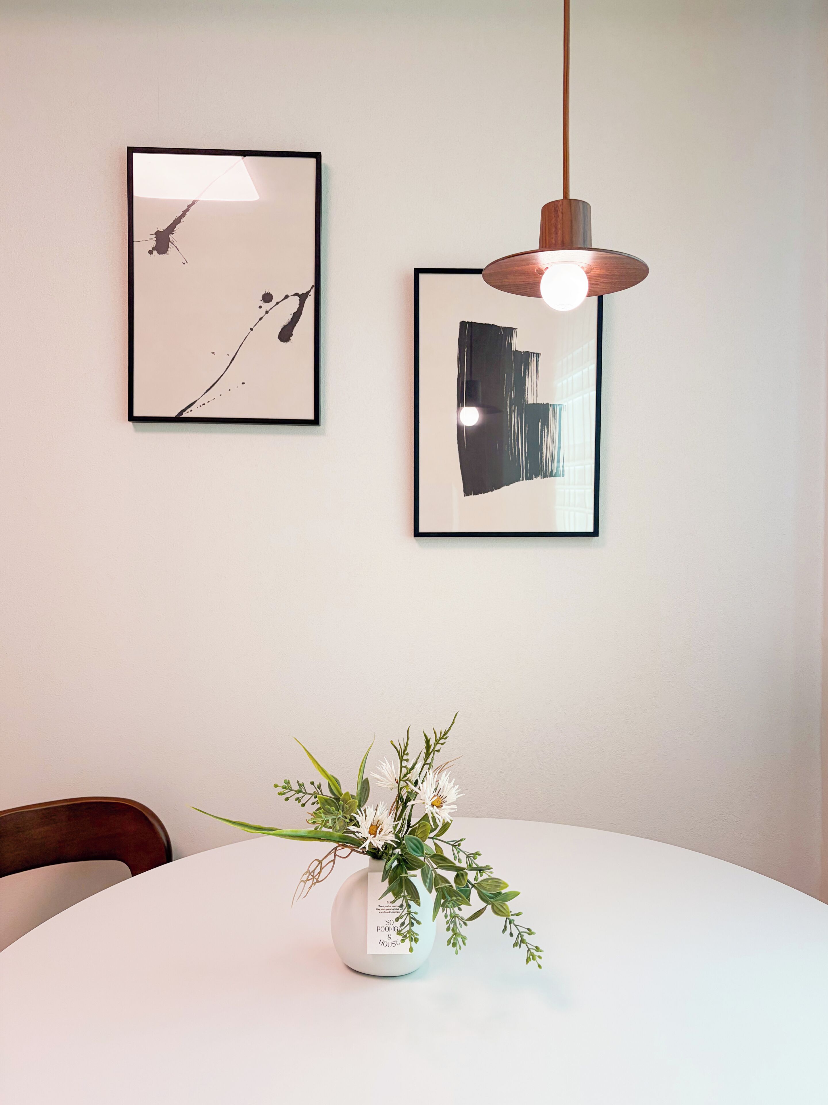 A dining area with a white table, a vase with flowers, and two framed artworks on the wall.