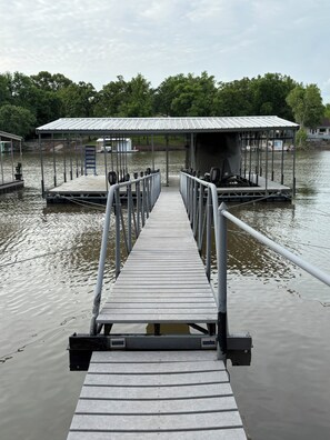 A wooden dock leading to a covered boat launch area with a metal railing. - Lake front house on Monkey Island with private dock (Afton)