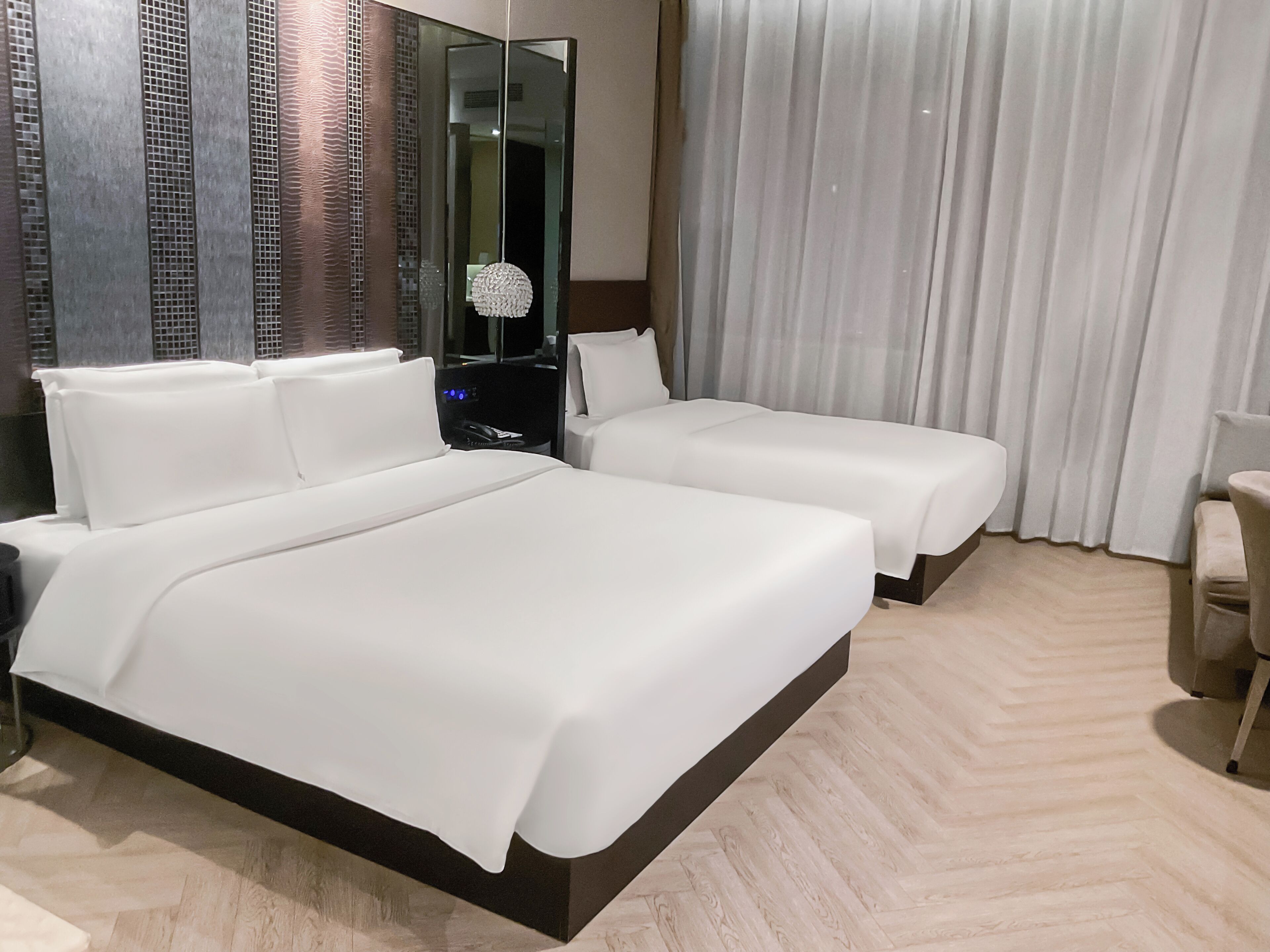 Habitación de hotel con una cama grande, una mesita de noche, un espejo, una silla y vistas a la ciudad.