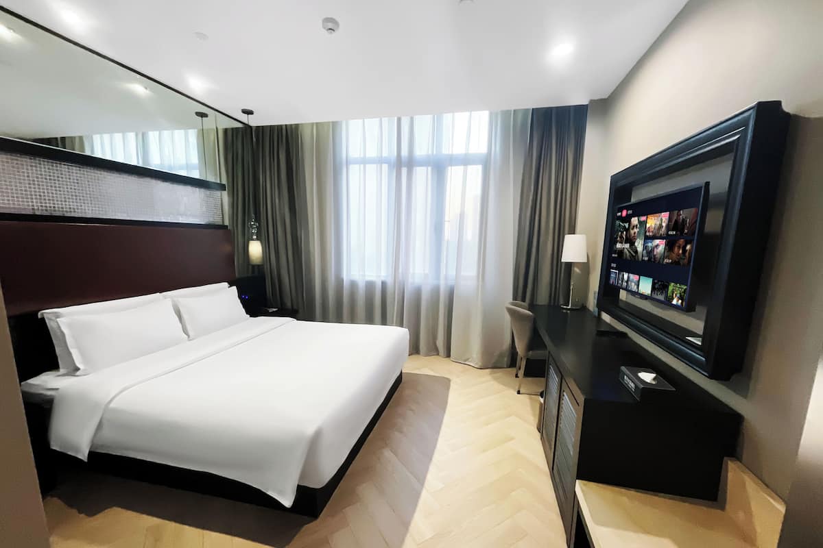 Una habitación de hotel con una cama, televisor, escritorio y ventana con cortinas.