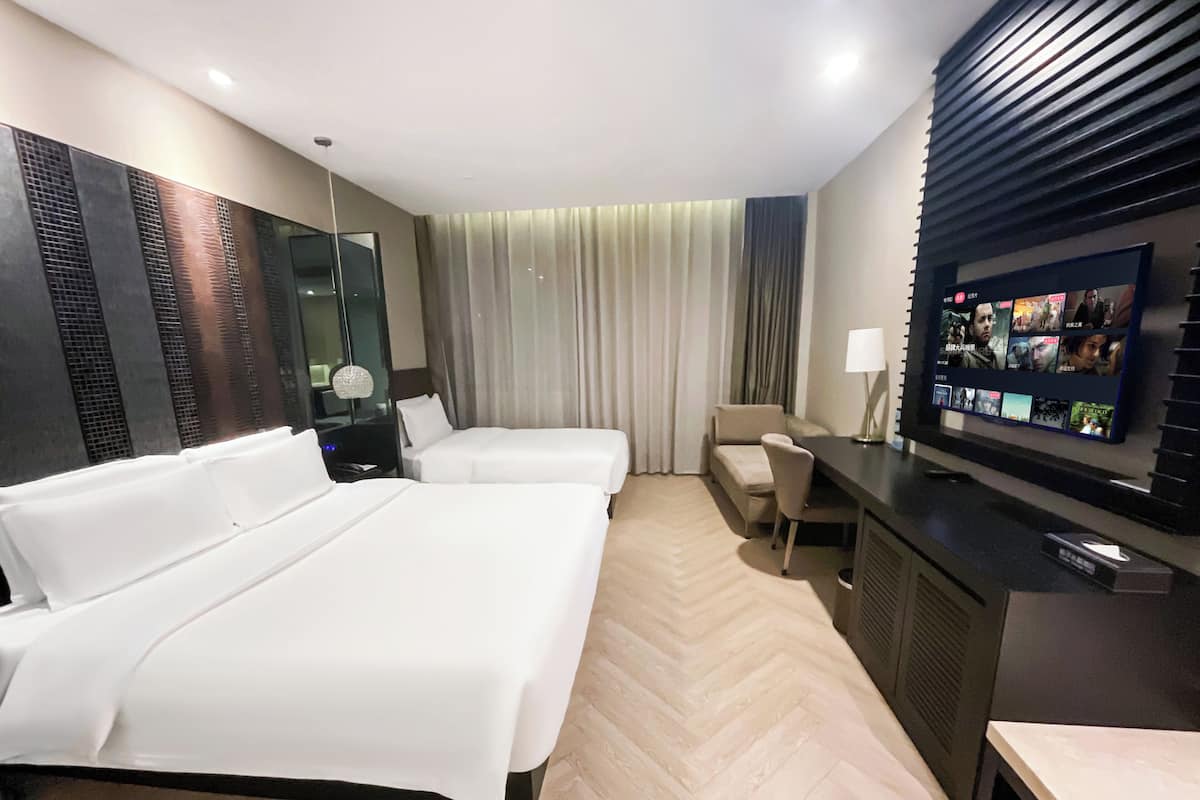Habitación de hotel con dos camas, un escritorio con televisor y un ventanal con cortinas.